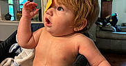 Elias joined the competition — help win amazing prizes! baby, child, high_chair, kitchen, table, snack, chip, wet_skin, curly_hair, indoor, home, furniture, face, expression, looking_up, curious, sitting, arm, mouth_open, light