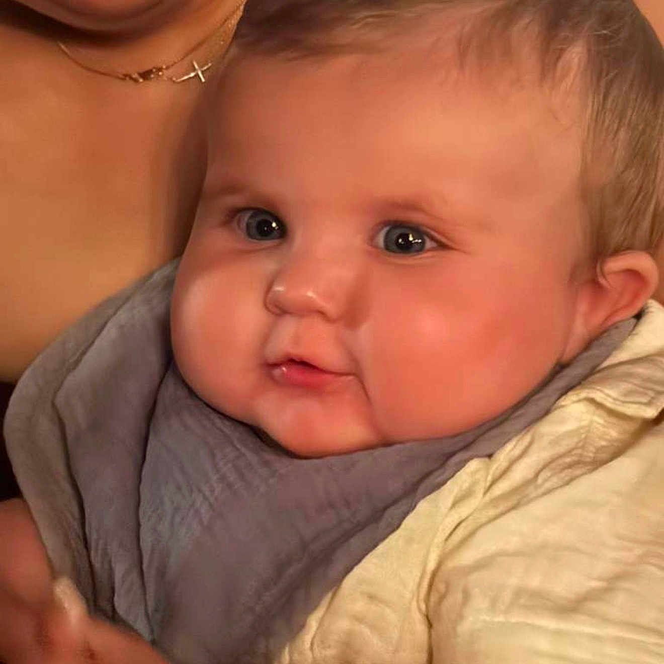 Alexander joined the competition — help win amazing prizes! baby, child, face, closeup, bib, clothing, skin, cheeks, eyes, mouth, expression, person, portrait, infant, cute, young, holding, adult, necklace, soft_lighting