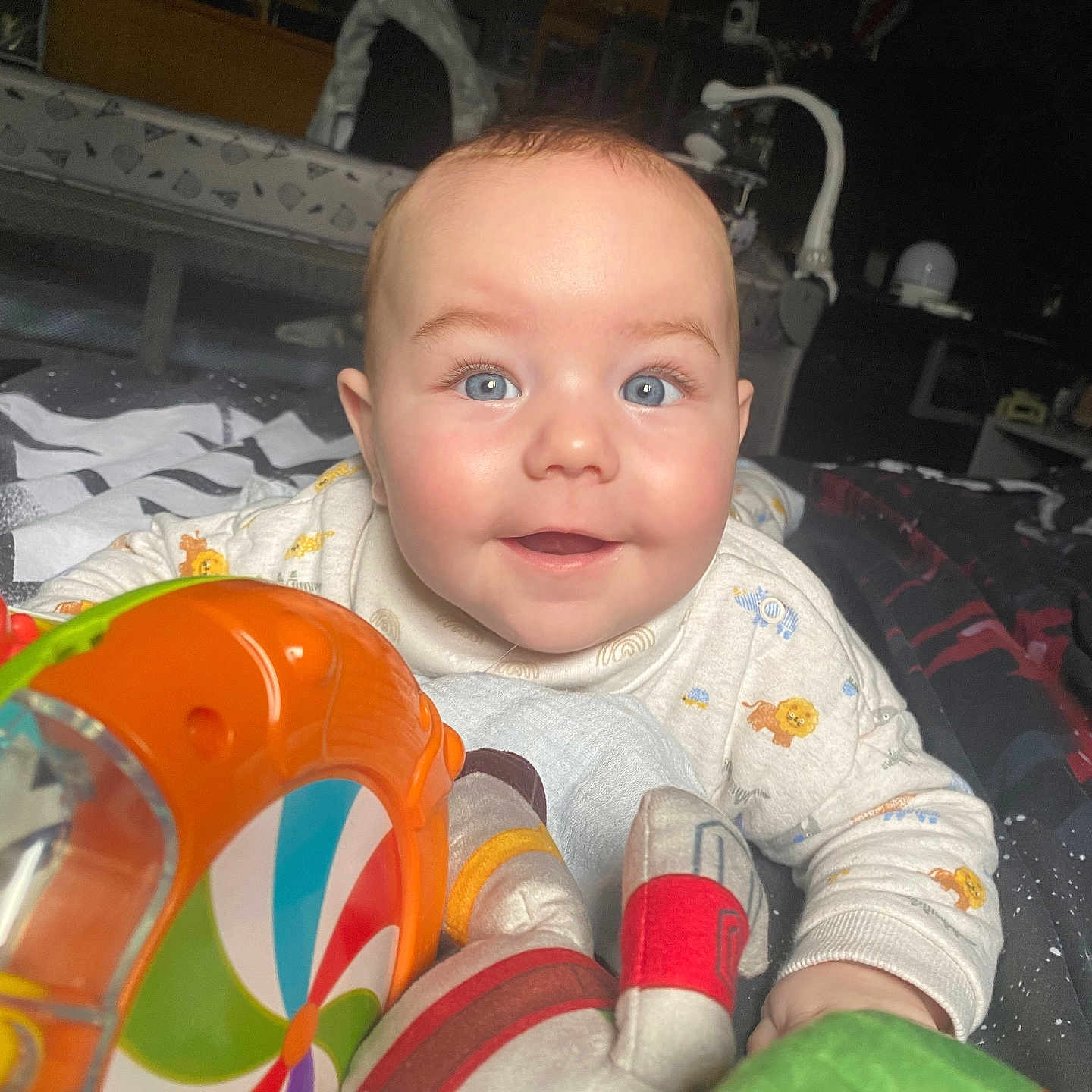 Reuben is registered to the contest to win money with this photo: baby, bed, blanket, blue_eyes, cheeks, child, closeup, clothing, colorful, cute, face, happy, head, indoor, infant, patterned, person, playful, smile, toy