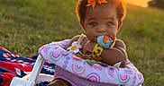 Leyah is registered to the contest to win money with this photo: baby, infant, child, curly_hair, orange_bow, outdoor, sunset, grass, baby_seat, blanket, toy, wristband, cute, smiling, nature, sunlight, portrait, sitting, face, happy