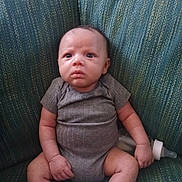 Ezekiel is registered to the contest to win money with this photo: baby, infant, child, onesie, bottle, couch, upholstery, sitting, socks, portrait, eyes, hands, legs, face, head, indoor, furniture, skin, curious_expression, newborn