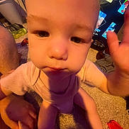 Willow is registered to the contest to win money with this photo: baby, child, hand, carpet, television, cartoon, indoor, person, clothing, pink, face, adult_hand, sitting, closeup, screen, toy, floor, curious, home, infant