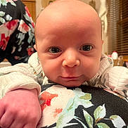 Liam is registered to the contest to win money with this photo: baby, infant, face, hand, closeup, indoor, floral_pattern, clothing, person, expression, skin, window, wooden_blinds, furniture, warm_lighting, background, curious, newborn, portrait, soft_texture
