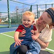 Henry joined the competition — help win amazing prizes! baby, child, adult, woman, smile, happy, overalls, denim, sneakers, tennis_court, fence, outdoor, sky, sunny, portrait, holding, playful, headband, face, hand