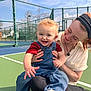 baby, child, adult, woman, smile, happy, overalls, denim, sneakers, tennis_court, fence, outdoor, sky, sunny, portrait, holding, playful, headband, face, hand