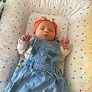 Ambre participe au concours pour gagner de l'argent avec cette photo : baby, infant, denim_dress, headband, orange, cushion, pattern, triangle, colorful, white_clothing, lying_down, wooden_chair, indoor, floor_tiles, furniture, newborn, cute, small_hands, portrait, person