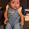 Ivy is registered to the contest to win money with this photo: baby, child, denim, overalls, pink, shirt, face, sitting, indoor, couch, living_room, person, curious, clothing, footwear, cute, hair_clip, wooden_floor, casual, home