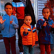 Malick a rejoint le concours — aidez-le/la à gagner de superbes lots ! child, adult, group, outdoor, jackets, sneakers, building, glass_door, hand_gesture, smile, emotion, scarf, tree, pavement, red_pants, blue_jacket, orange_jacket, casual_clothing, person, family