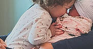 Luna is registered to the contest to win money with this photo: toddler, newborn, baby, child, curly_hair, floral_blanket, swaddled, kissing, family, love, affection, indoor, holding, person, closeup, intimate, caring, parent, sibling, cozy