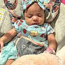 Nova is registered to the contest to win money with this photo: baby, sleeping, infant, headband, bow, blue_outfit, cartoon_characters, baby_seat, cushion, floral_pattern, blanket, soft_texture, child, cute, peaceful, indoors, clothing, person, resting, young
