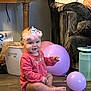 baby, balloons, casual, child, curious, cute, floor, headwear, household_items, indoor, infant, person, pink_dress, purple, relaxed, sitting, smiling, tiara, toy, wooden_floor