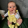baby, child, infant, yellow_outfit, yellow_socks, sitting, thumb_in_mouth, blue_eyes, curious_expression, green_surface, gray_background, indoor, cute, portrait, person, clothing, soft_lighting, close_up, face, head