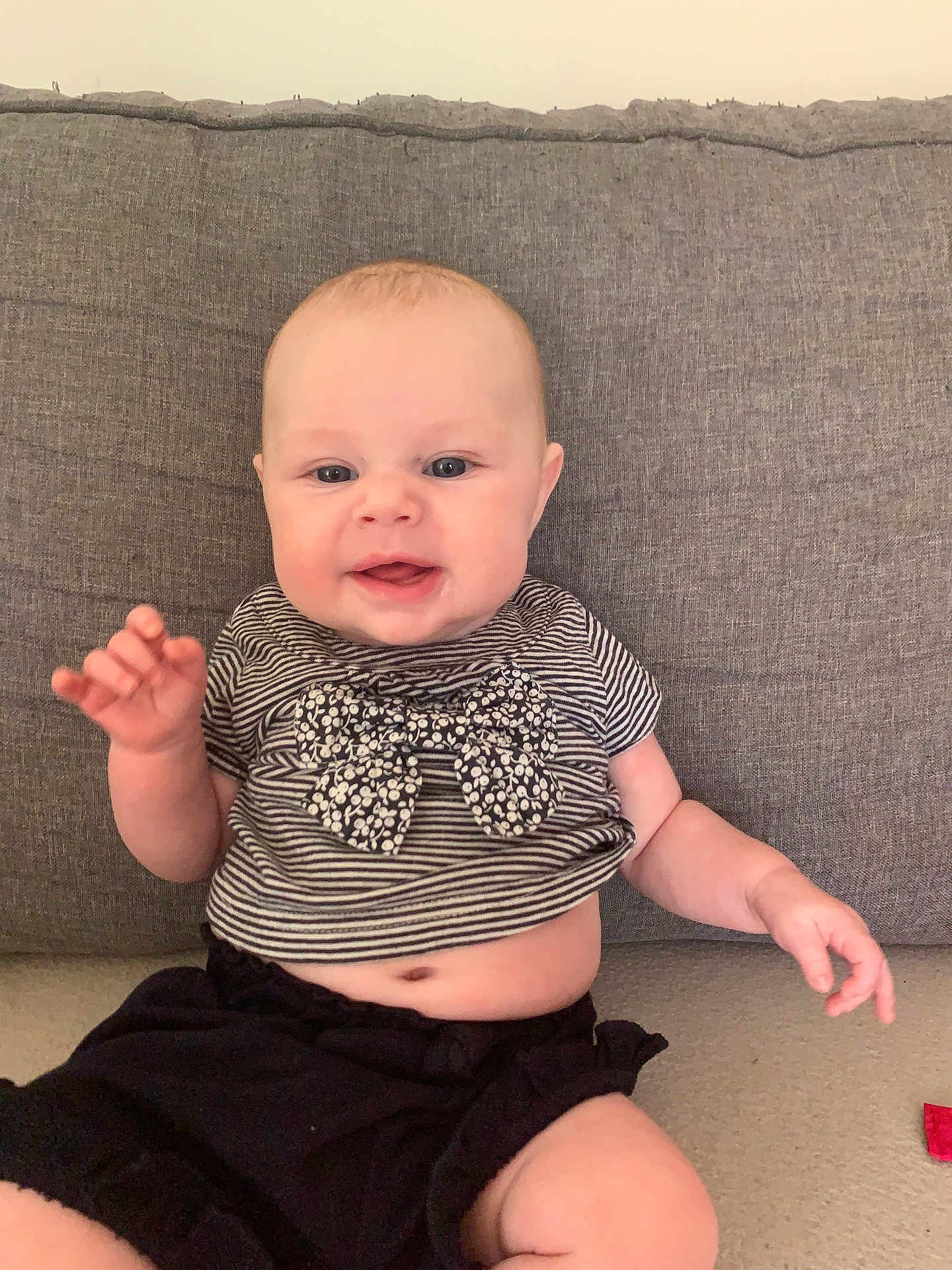 Maya a rejoint le concours — aidez-le/la à gagner de superbes lots ! baby, child, smiling, happy, couch, striped_shirt, bow, black_shorts, sitting, indoor, cute, face, hand, skin, person, infant, young_child, casual_clothing, furniture, home