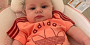 Maya participe au concours pour gagner de l'argent avec cette photo : baby, infant, child, adidas, clothing, red_shorts, orange_shirt, baby_seat, cushion, pillow, indoor, portrait, face, head, eyes, person, soft_toys, comfort, casual_wear, home