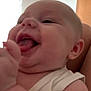 baby, infant, smiling, tongue_out, close_up, white_clothing, arm, face, happy, indoor, window, curtains, skin, person, child, head, mouth, ear, cheek, room