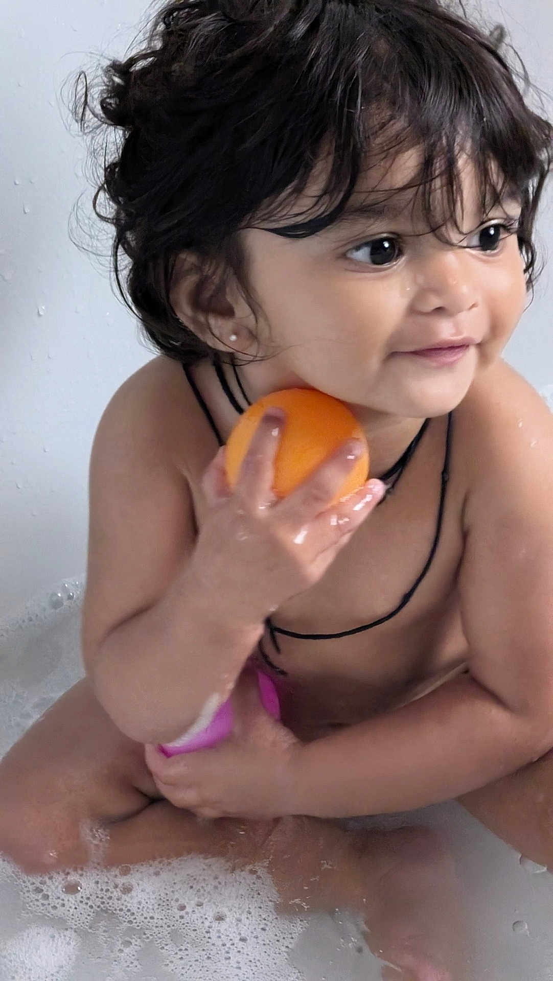 Aarvi is registered to the contest to win money with this photo: toddler, child, bathtub, water, bubbles, orange, toy, wet_hair, smiling, skin, earrings, black_string, bath_time, cute, happy, young_child, indoor, play, sitting, person