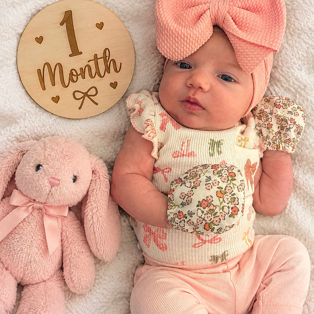 Kennedy joined the competition — help win amazing prizes! baby, infant, child, portrait, lying_down, pink, bow, headband, floral_outfit, onesie, plush_toy, bunny, stuffed_animal, milestone_sign, one_month, blanket, cozy, indoor, cute, photography