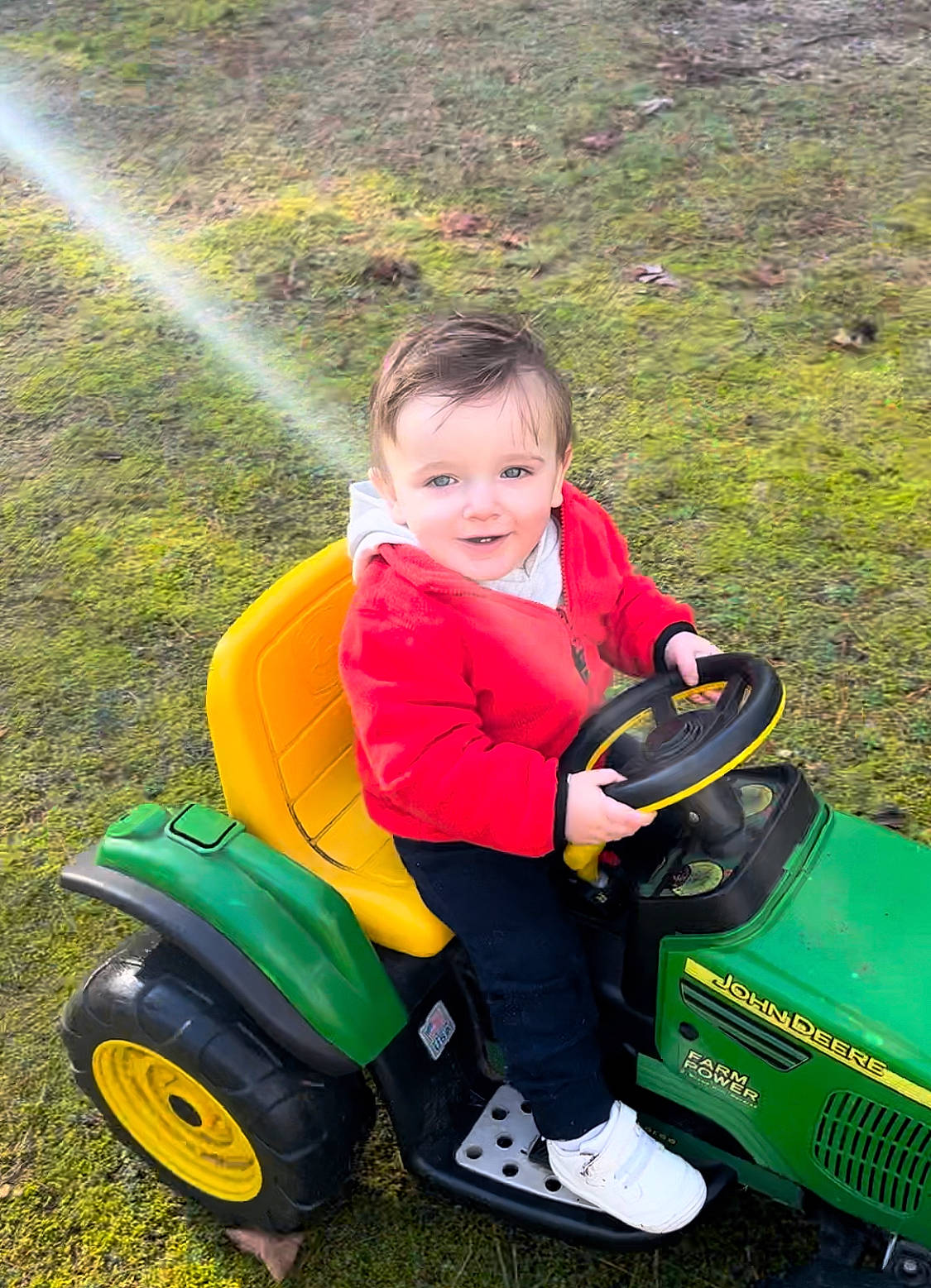 Austin is registered to the contest to win money with this photo: automotive_tire, field, fun, grass, grassland, green, joy, land_vehicle, lawn, mode_of_transport, motor_vehicle, nature, people_in_nature, person, plant, rainbow, recreation, riding_toy, tire, toddler
