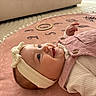 baby, infant, headband, pink, smile, play_mat, clothing, face, child, cute, lying_down, indoor, soft_texture, eyes, happy, button, fabric, head, person, toddler