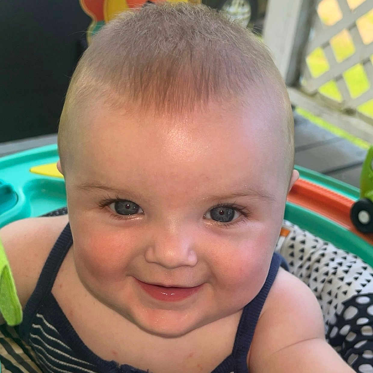 Eliza joined the competition — help win amazing prizes! arm, baby, cheeks, child, closeup, clothing, colorful, eyes, face, happy, infant, outdoor, play_area, porch, seat, skin, smiling, striped, sunlight, toy