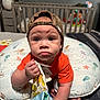 baby, child, cap, drool, pillow, crib, toy, cloth_book, orange_shirt, camo, indoor, floor, striped_rug, cute, infant, pout, wide_eyes, hand, sitting, nursery
