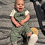 baby, smiling, green_overalls, checkered_shoes, blanket, happy, infant, cute, child, footwear, texture, pattern, knit, fabric, indoor, portrait, hands, sitting, face, apparel