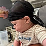baby, child, headscarf, striped_shirt, indoor, person, hand, table, chair, cup, curious, side_view, holding, infant, skin, young_child, casual_clothing, closeup, portrait, soft_lighting