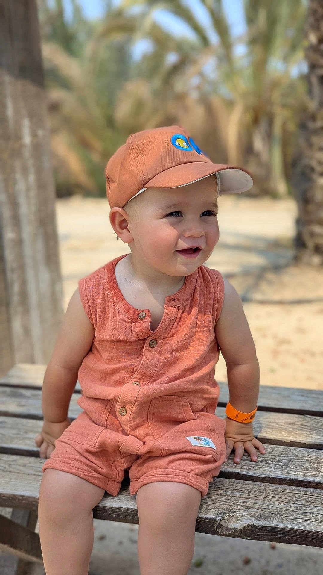 Simon a rejoint le concours — aidez-le/la à gagner de superbes lots ! toddler, child, smiling, outdoor, bench, cap, orange_clothing, shorts, sleeveless, sunny, daylight, palm_trees, nature, skin, happy, portrait, sitting, baby, cute, summer