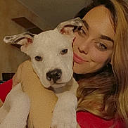 Lil P is registered to the contest to win money with this photo: woman, dog, puppy, hugging, indoor, red_shirt, long_hair, white_dog, pet, face, smile, close_up, affection, cute, animal, person, portrait, looking, ears, black_nose