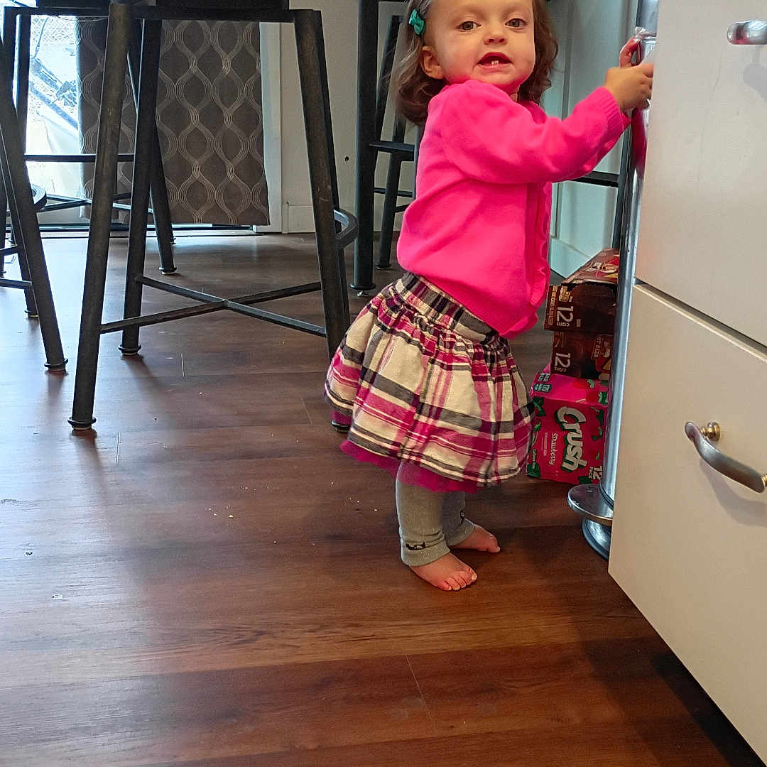 Nena joined the competition — help win amazing prizes! barefoot, cabinet, chair, child, curtain, expression, flooring, furniture, hair_clip, holding, home, indoor, kitchen, person, pink_sweater, plaid_skirt, standing, toddler, wooden_floor, young_child