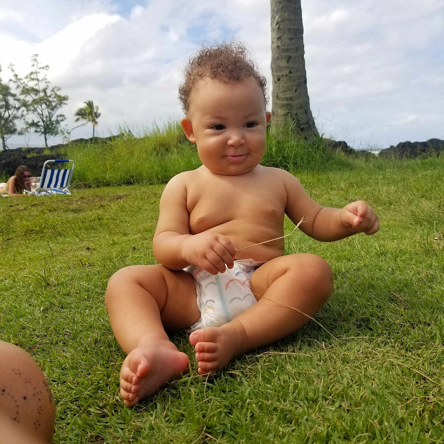 Lalu is registered to the contest to win money with this photo: baby, barefoot, beach, chair, child, clouds, curly_hair, diaper, grass, grass_blade, infant, nature, outdoors, palm_tree, portrait, sitting, sky, smiling, sunlight, tropical