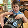 child, boy, wheelchair, indoor, bucket, halloween, pumpkin, tombstone, decorations, wooden_floor, cabinet, light, window, door, shorts, blue_shirt, furniture, person, curtains, plastic_bucket