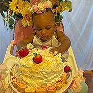 Ailai is registered to the contest to win money with this photo: baby, child, cake, strawberries, high_chair, flower_crown, flowers, cream, birthday, celebration, decorations, curious, cute, indoor, plate, wooden_floor, pink_chair, gold_chain, hand, foot