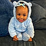 baby, blue_onesie, bow, child, couch, cozy, cute, face, fluffy_clothing, happy, headwear, home, indoor, infant, pillow, portrait, sitting, smiling, soft_texture, toddler