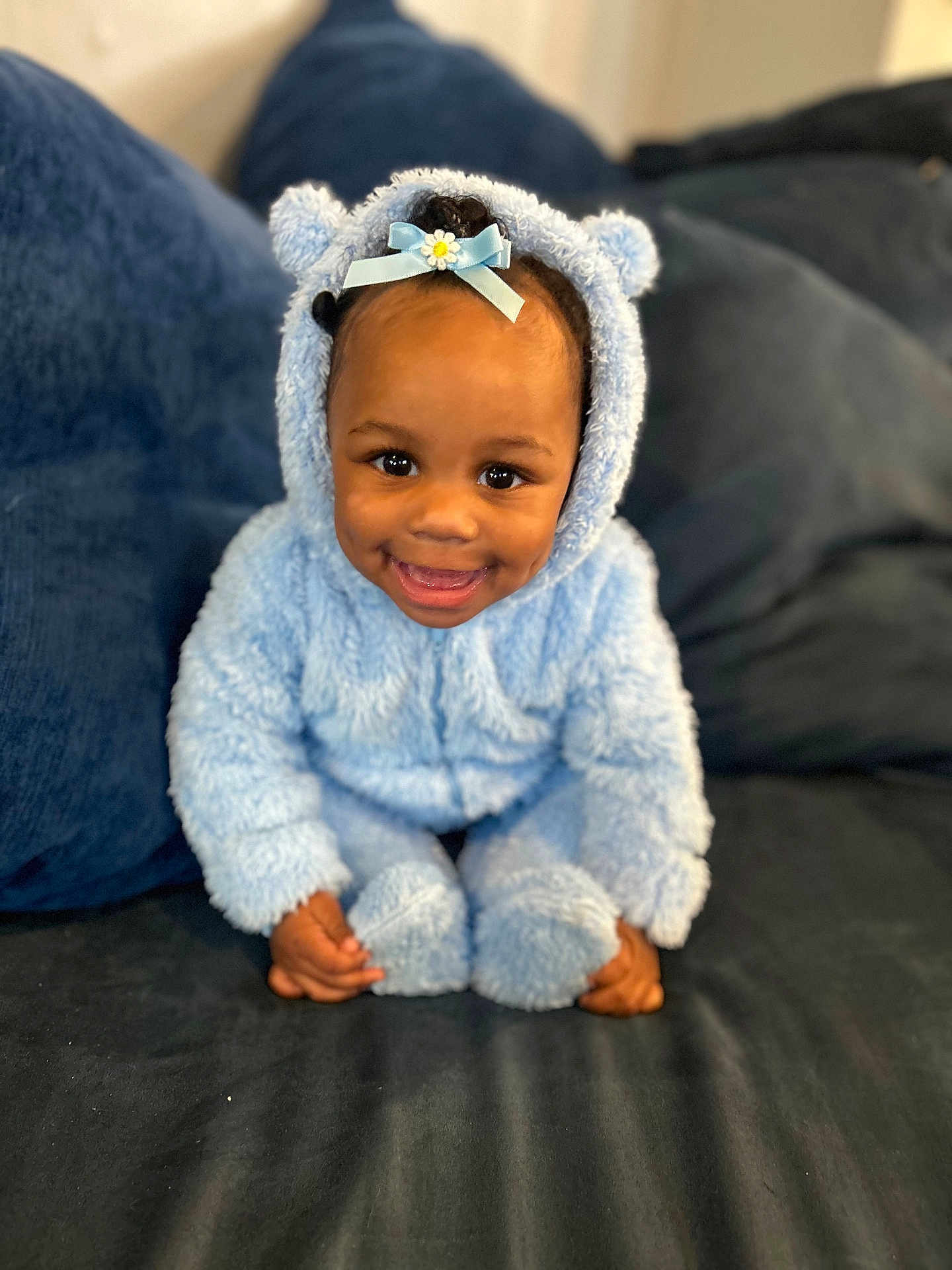 Ailai is registered to the contest to win money with this photo: toddler, child, smiling, blue_onesie, fluffy_clothing, bow, cute, baby, couch, pillow, indoor, portrait, happy, sitting, face, headwear, cozy, soft_texture, home, infant