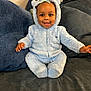 apparel, baby, blue_onesie, child, couch, cozy, cute, dimples, face, fluffy_clothing, happy, home, indoor, infant, person, pillow, portrait, seated, smile, soft_texture