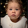 toddler, child, portrait, baby, face, eyes, hair, curly_hair, white_vest, soft_lighting, indoor, holiday_lights, background_bokeh, cute, innocent, expression, close_up, winter_clothing, studio_photo, warm_tones