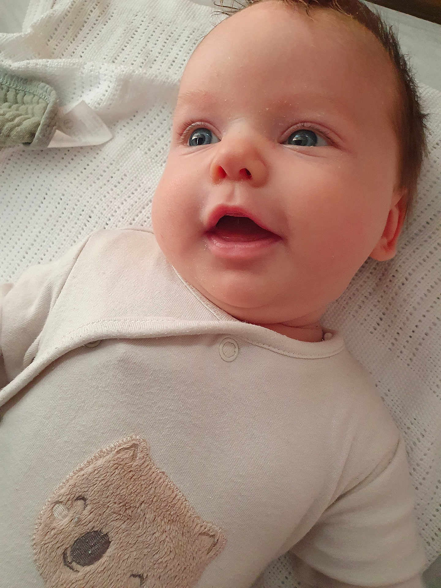 Harrison is registered to the contest to win money with this photo: baby, infant, face, eyes, mouth, onesie, clothing, bear_patch, blanket, texture, cute, smiling, child, person, portrait, indoor, skin, head, happy, closeup