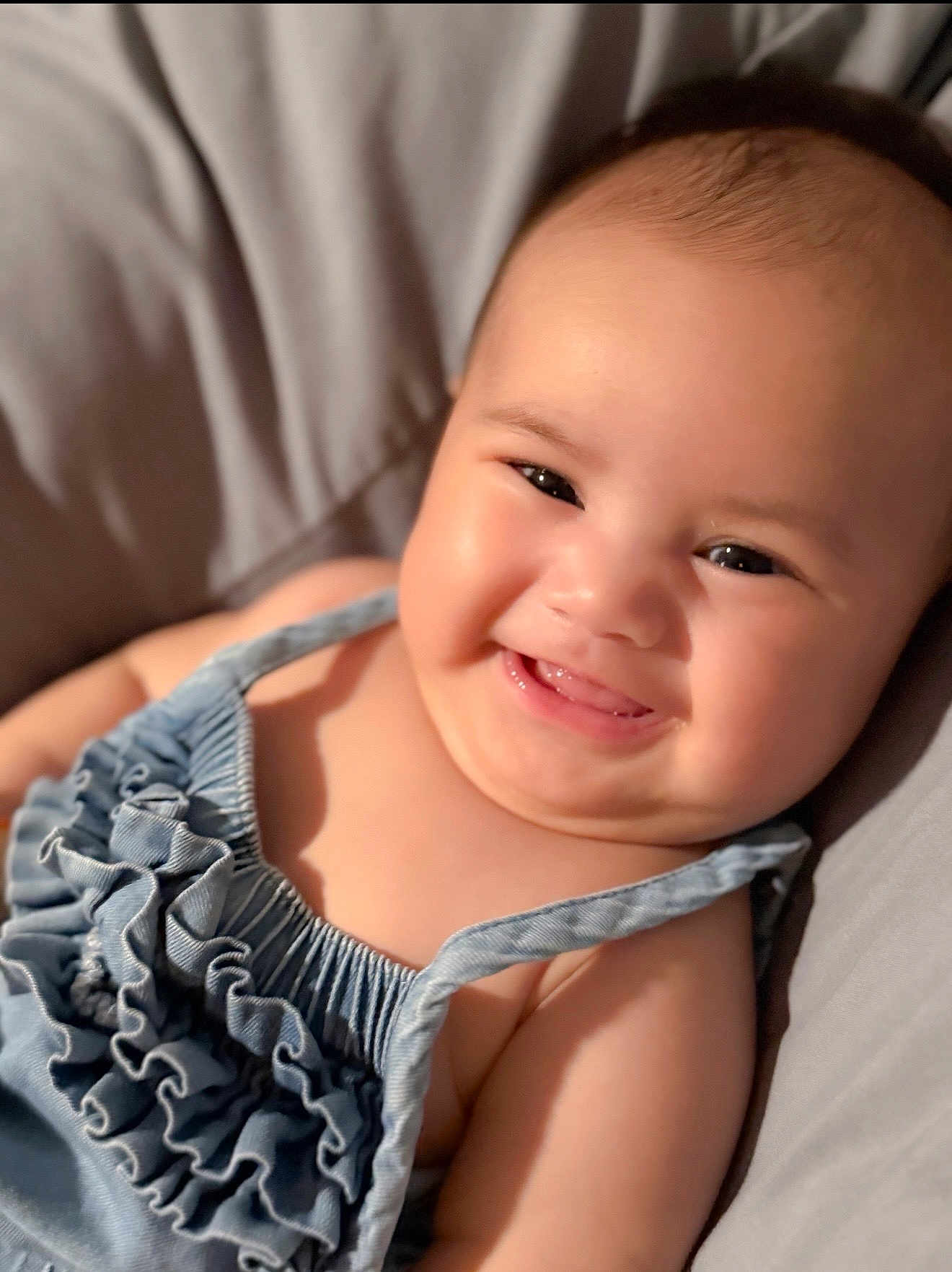 Zuri is registered to the contest to win money with this photo: baby, child, smiling, face, skin, clothing, blue, ruffles, cheeks, tongue, happy, infant, portrait, closeup, soft, bed, cushion, cute, person, indoors