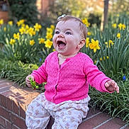 Elody is registered to the contest to win money with this photo: baby, brick_ledge, child, cute, earrings, face, grass, greenery, happy, laughing, nature, outdoor, patterned_pants, person, pink_sweater, portrait, smile, sunlight, toy, yellow_flowers