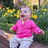 baby, child, pink_sweater, patterned_pants, brick_ledge, yellow_flowers, greenery, outdoor, happy, laughing, toy, grass, nature, sunlight, cute, portrait, person, face, smile, earrings