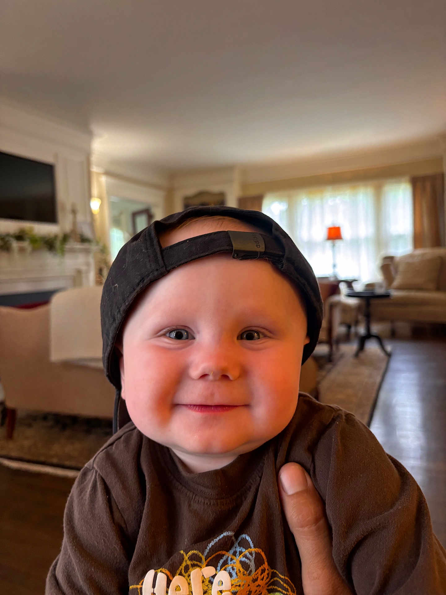Canaan is registered to the contest to win money with this photo: baby, child, smiling, cap, indoor, living_room, furniture, hand, person, cute, portrait, brown_shirt, cozy, cheeks, headwear, happy, home, toddler, face, casual