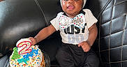 Raylan joined the competition — help win amazing prizes! baby, child, birthday_cake, candle, black_leather_couch, clothing, hat, socks, celebration, smiling, indoor, person, happy, food, cake, party, home, cute, infant, two_months