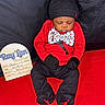 Raylan is registered to the contest to win money with this photo: baby, infant, sleeping, red_clothing, black_clothing, hat, mittens, bow_tie, sign, birth_details, blanket, portrait, indoors, resting, cute, newborn, child, baby_clothes, baby_shoes, one_month