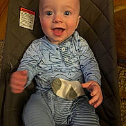Rhys is registered to the contest to win money with this photo: baby, smiling, infant, dinosaur_pajamas, striped_pants, sock, baby_seat, cushion, happy, child, person, indoors, wood_floor, clothing, cute, portrait, hand, face, expression, seated