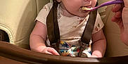 Kaylynn is registered to the contest to win money with this photo: baby, high_chair, feeding, spoon, food, child, infant, meal, curious, beige, plastic_bowl, hand, table, clothing, straps, indoor, closeup, face, expression, messy