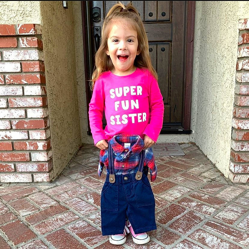 Cooper is registered to the contest to win money with this photo: arm, baby_toddler_clothing, brick, brickwork, clothing, electric_blue, eye, face, happy, head, person, photograph, pink, sleeve, smile, standing, street_fashion, t_shirt, textile, toddler