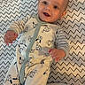 baby, infant, smile, onesie, dog_pattern, zigzag_pattern, blanket, happy, lying_down, cute, child, face, hand, clothing, baby_wipes, indoor, portrait, young_child, playful, bright_eyes