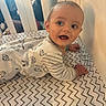 baby, crib, onesie, patterned_clothing, zigzag_pattern, infant, child, face, expression, crawling, bedroom, furniture, white_crib, young_child, indoors, person, cute, looking_away, hand, smiling
