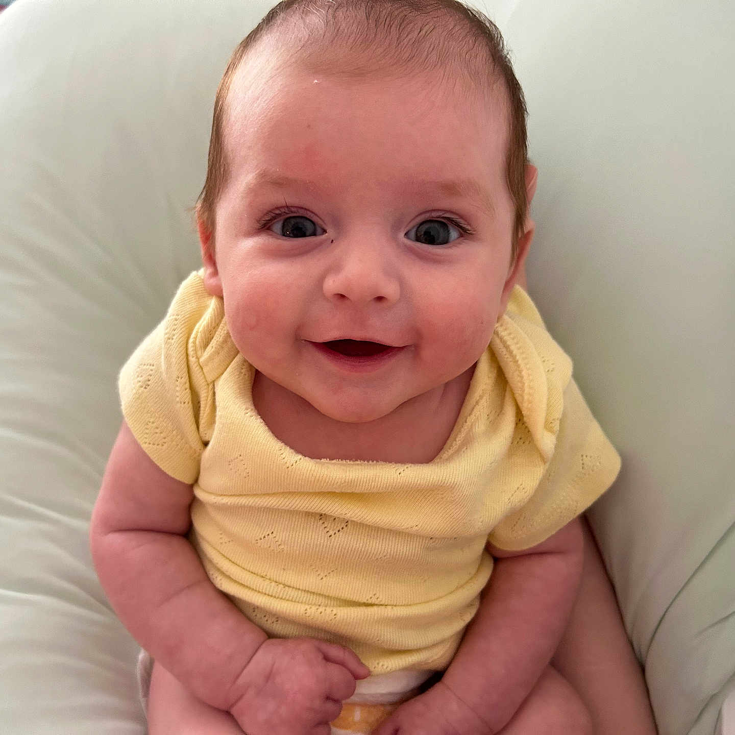 Cello is registered to the contest to win money with this photo: baby, bright_eyes, child, closeup, cushion, cute, face, happy, head, indoors, infant, person, plush, portrait, sitting, skin, small_hands, smiling, yellow_clothing, young